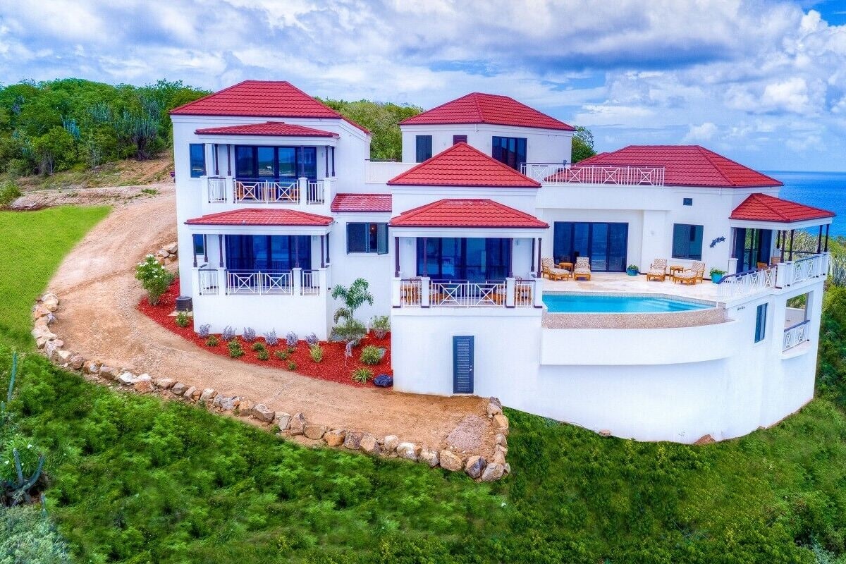 Una casa blanca de varios pisos con tejados rojos, una piscina y vistas al océano.