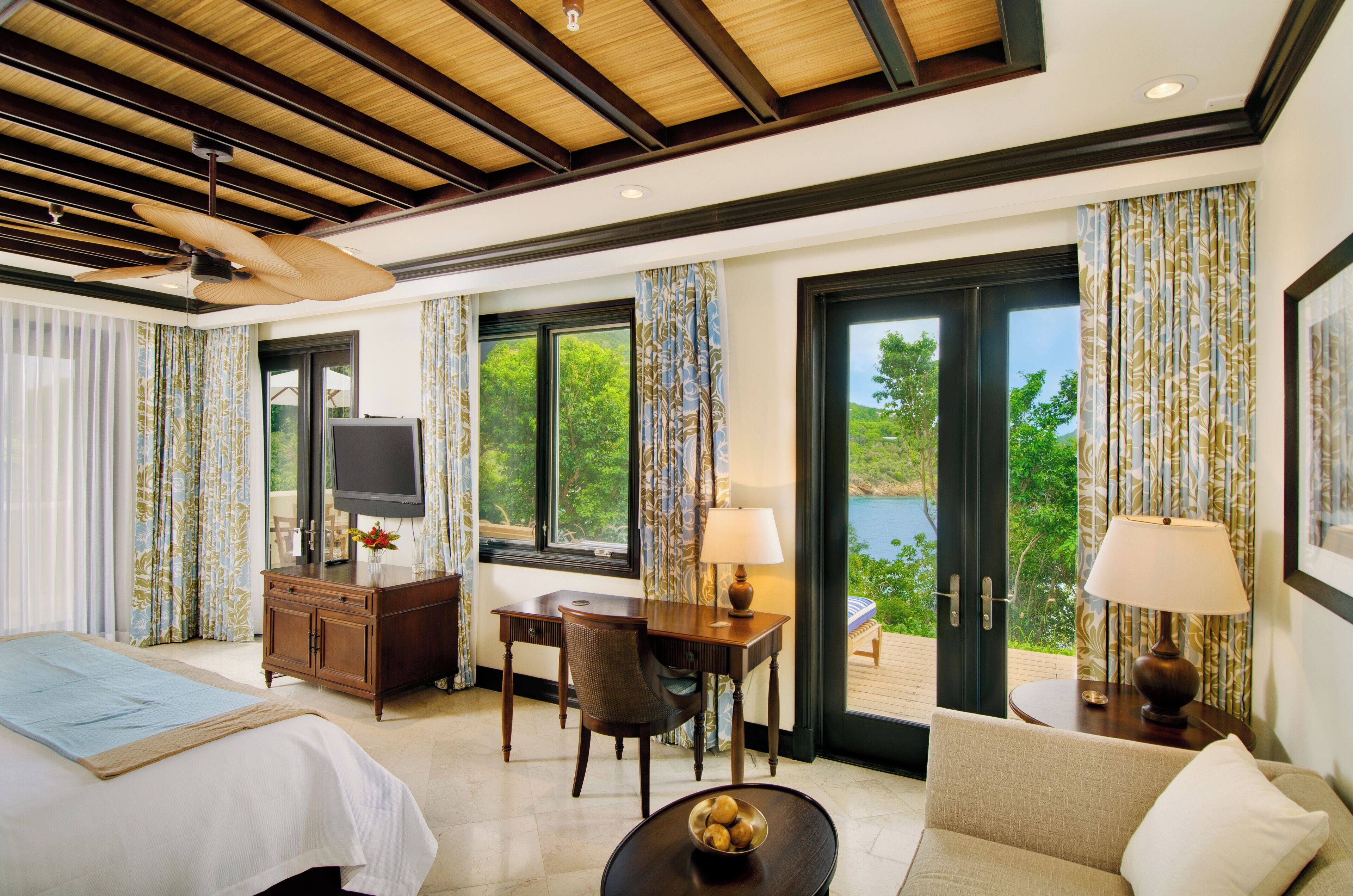 A hotel room with a bed, a desk, a chair, a TV, and a view of the outdoors.