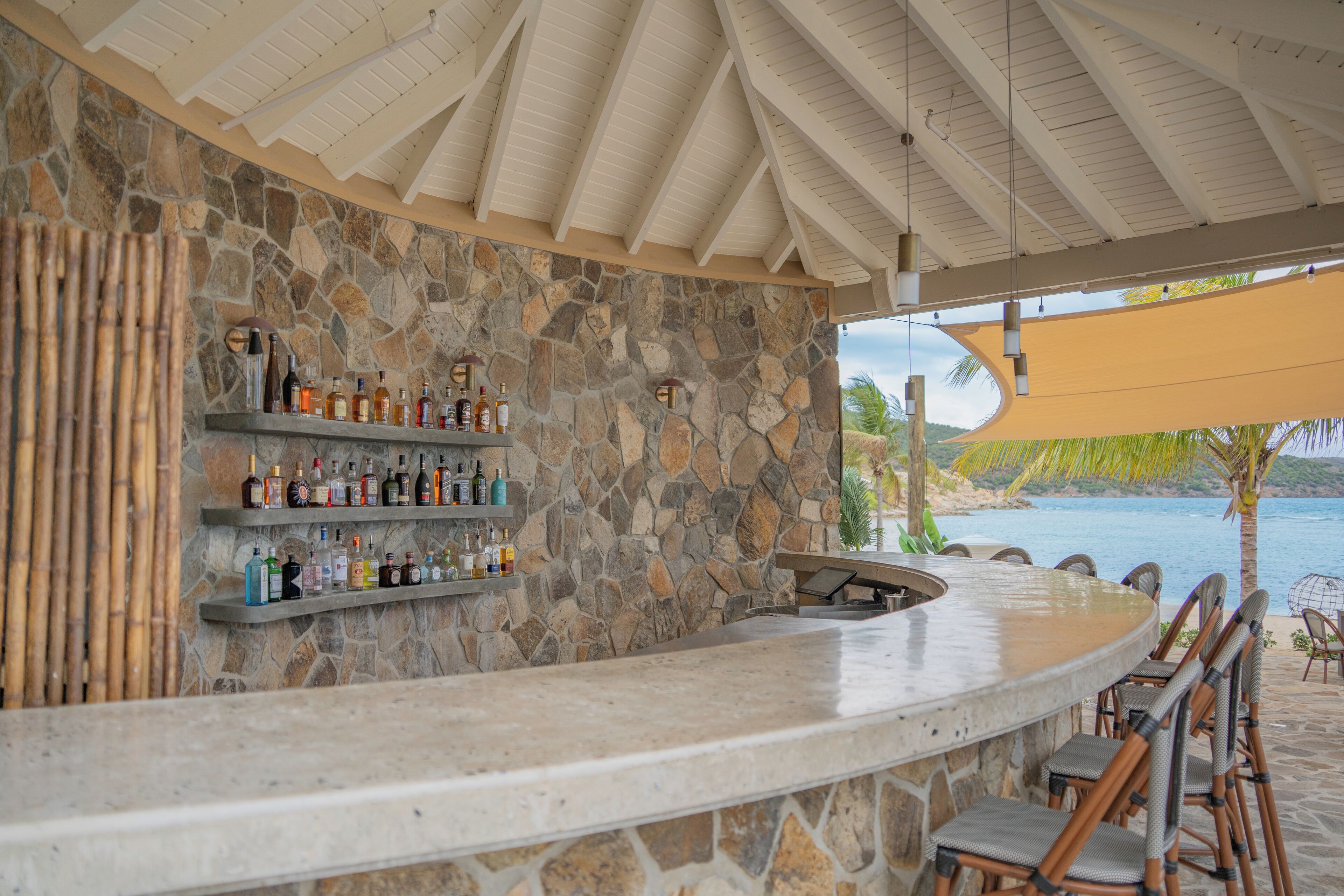 Una zona de bar con pared de piedra, estanterías con botellas y una barra curva.
