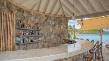 Una zona de bar con pared de piedra, estanterías con botellas y una barra curva.