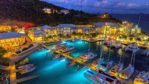 A marina with multiple boats docked, a swimming pool, and buildings with illuminated exteriors. - Scrub Island Resort, Spa & Marina (Scrub Island)