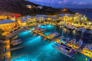 Puerto deportivo con varias embarcaciones amarradas, una piscina y edificios con fachadas iluminadas.