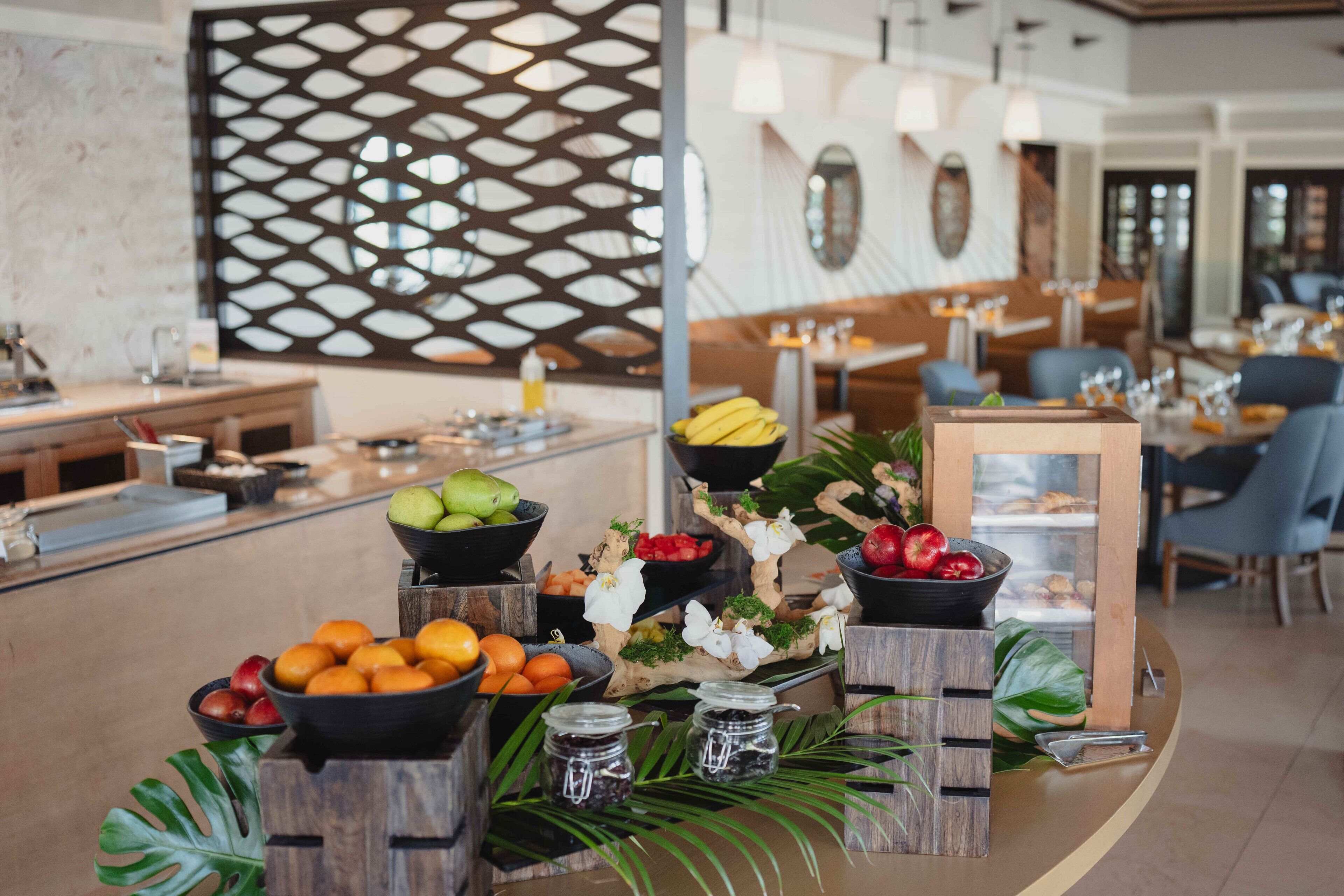 A buffet setup with various fruits, a decorative wall, and a seating area in a modern dining room.