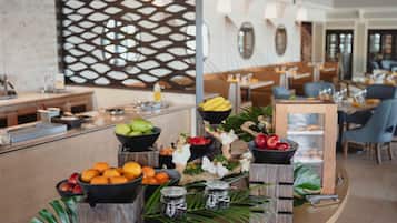 A buffet setup with various fruits, a decorative wall, and a seating area in a modern dining room.