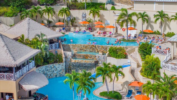 A resort with a large pool area, multiple levels of water features, and numerous sun loungers with umbrellas. - Scrub Island Resort, Spa & Marina (Scrub Island)