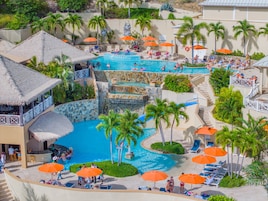Un resort con un amplio espacio de piscina, múltiples niveles de fuentes de agua y numerosas tumbonas con sombrillas.