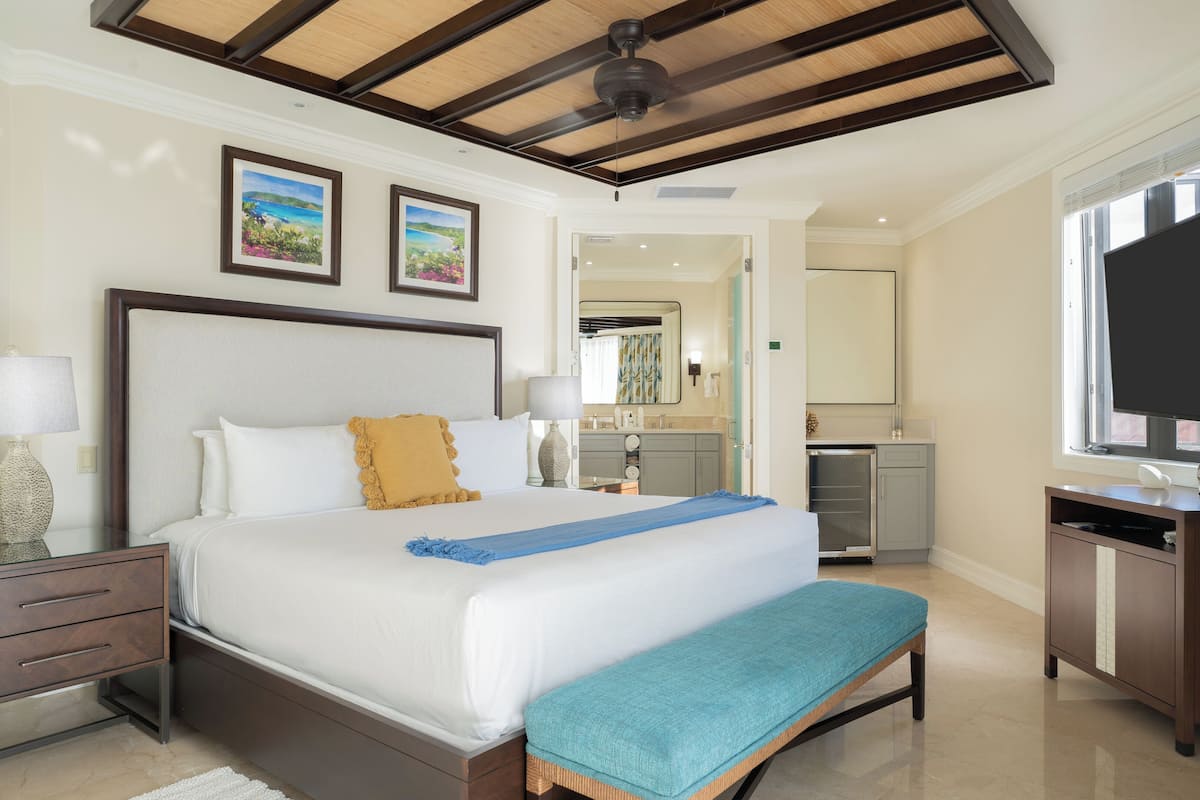 Habitación de hotel con una cama grande, mesitas de noche, un escritorio con televisor y un baño visible a través de una puerta abierta.