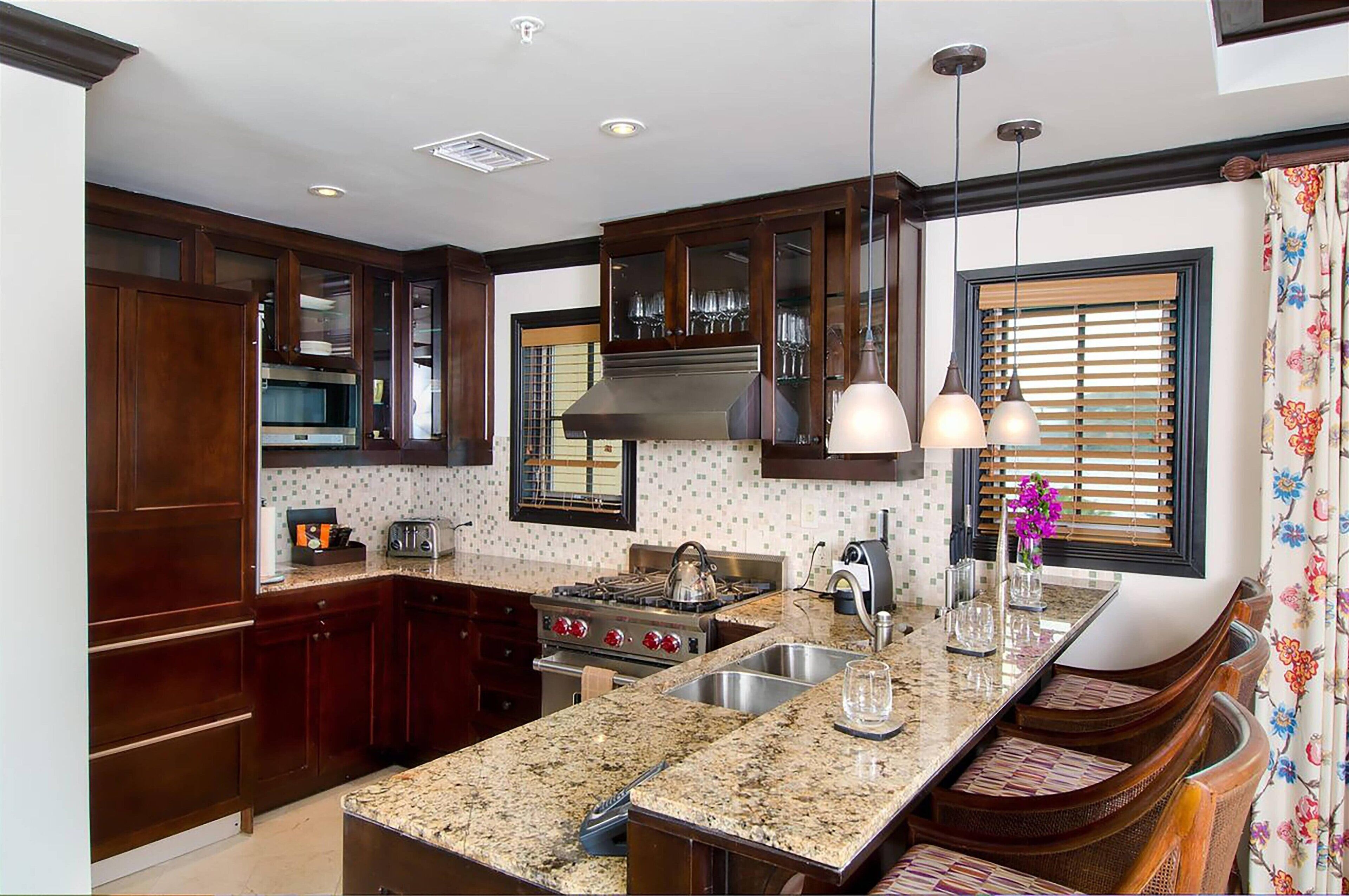 A kitchen with dark wood cabinets, a granite countertop, stainless steel appliances, and a window with blinds.