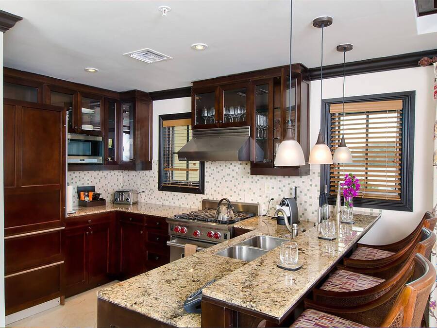 A kitchen with dark wood cabinets, a granite countertop, stainless steel appliances, and a window with blinds.