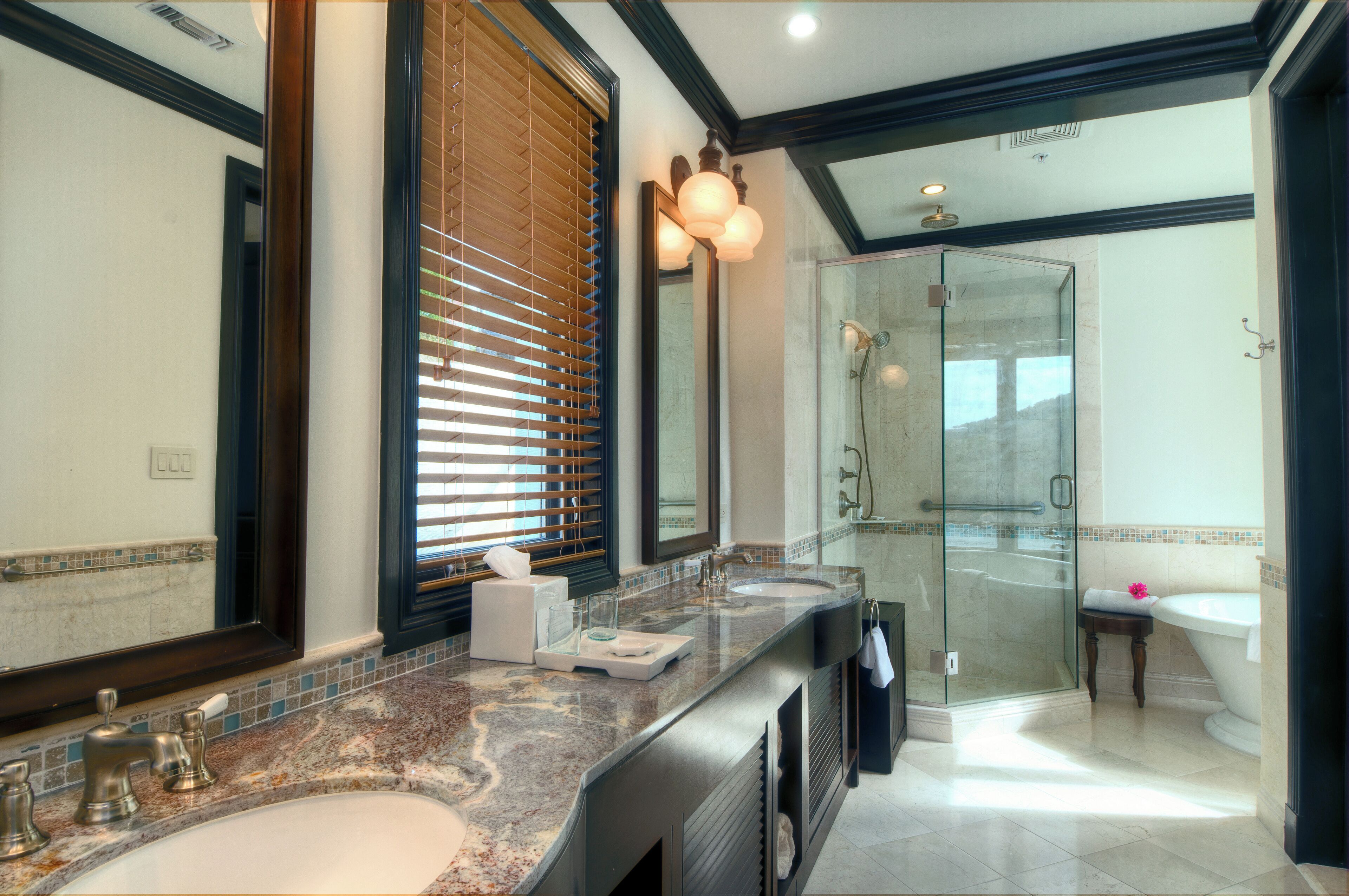 A modern bathroom with a large mirror, dual sinks, a glass shower enclosure, and a vanity with a marble countertop.