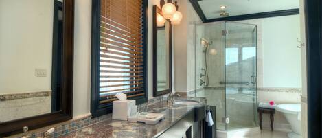 A modern bathroom with a large mirror, dual sinks, a glass shower enclosure, and a vanity with a marble countertop.