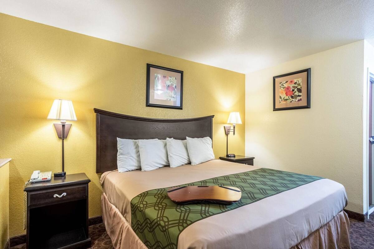 A hotel room with a bed, two bedside lamps, a telephone, and two framed pictures on the walls.