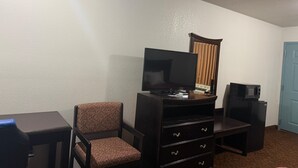 A room with a television on a stand, a chair, a small table, and a blue door. - The Magnolia Hotel Searcy (Searcy)