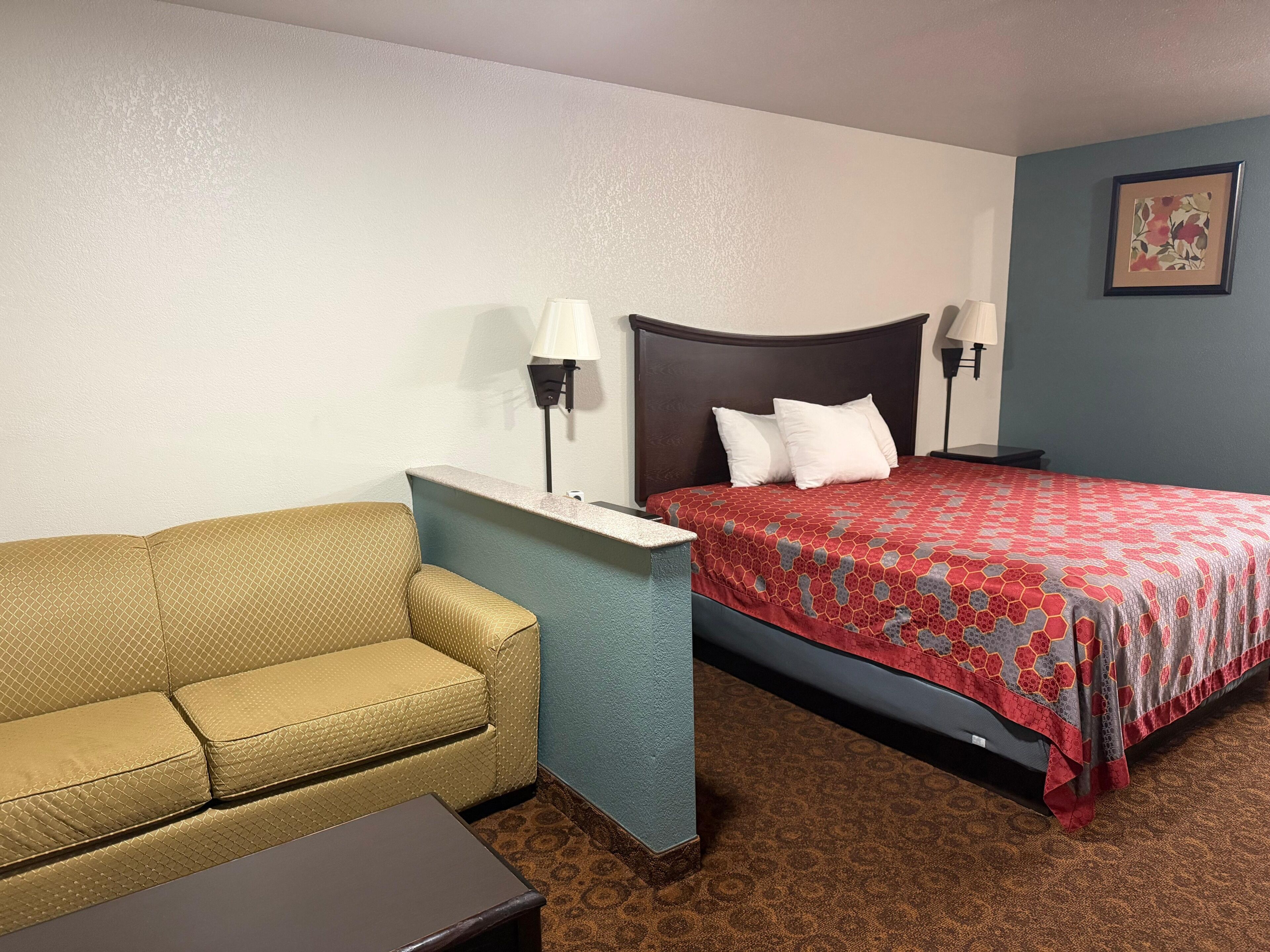 A hotel room with a bed, a sofa, a nightstand, and two wall-mounted lamps.