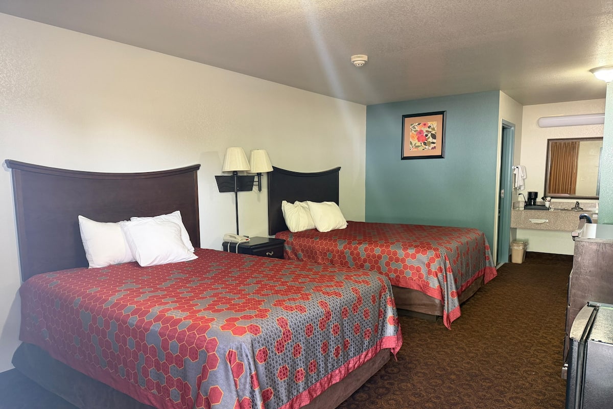 A hotel room with two beds, a desk, a lamp, a phone, and a mirror.