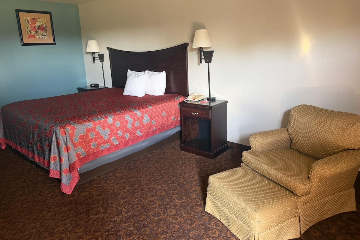 A hotel room with a bed, two bedside lamps, a nightstand, a chair, and a framed picture on the wall.