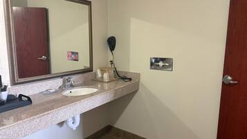 Een badkamer met een wastafel, spiegel, haardroger en een deur.