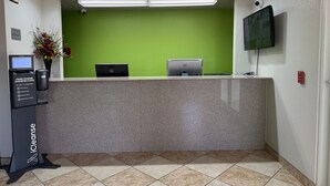 A reception desk with a green wall, a Dell computer, a monitor, a phone station, and a fire alarm. - The Magnolia Hotel Searcy (Searcy)