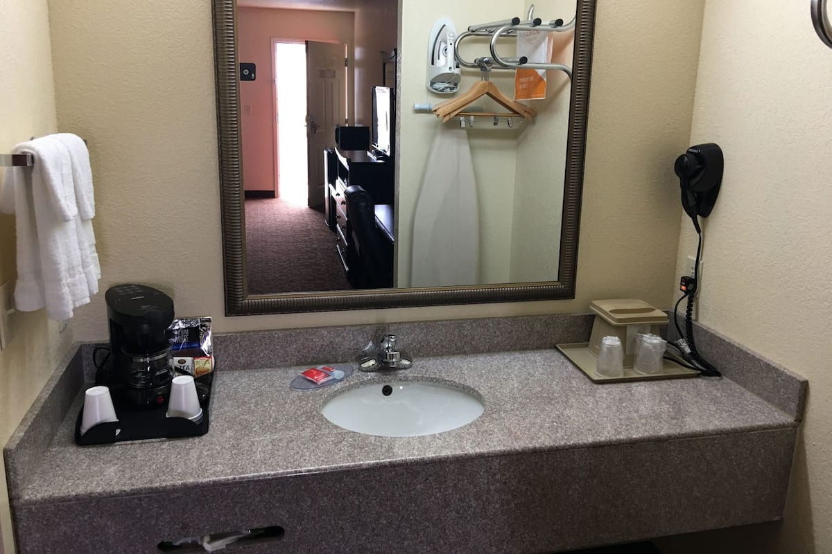 A bathroom with a sink, mirror, towel rack, and a coffee maker.