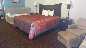 A hotel room with a bed, two bedside lamps, a chair, a small table, a bathroom with a bathtub, and a picture on the wall. - The Magnolia Hotel Searcy (Searcy)