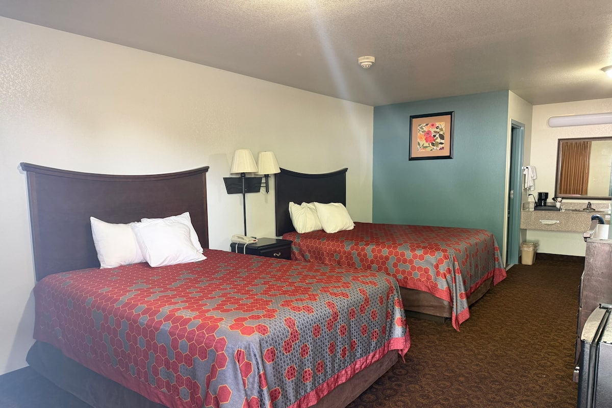 A hotel room with two beds, a nightstand, a lamp, a small table, a mirror, and a picture on the wall.