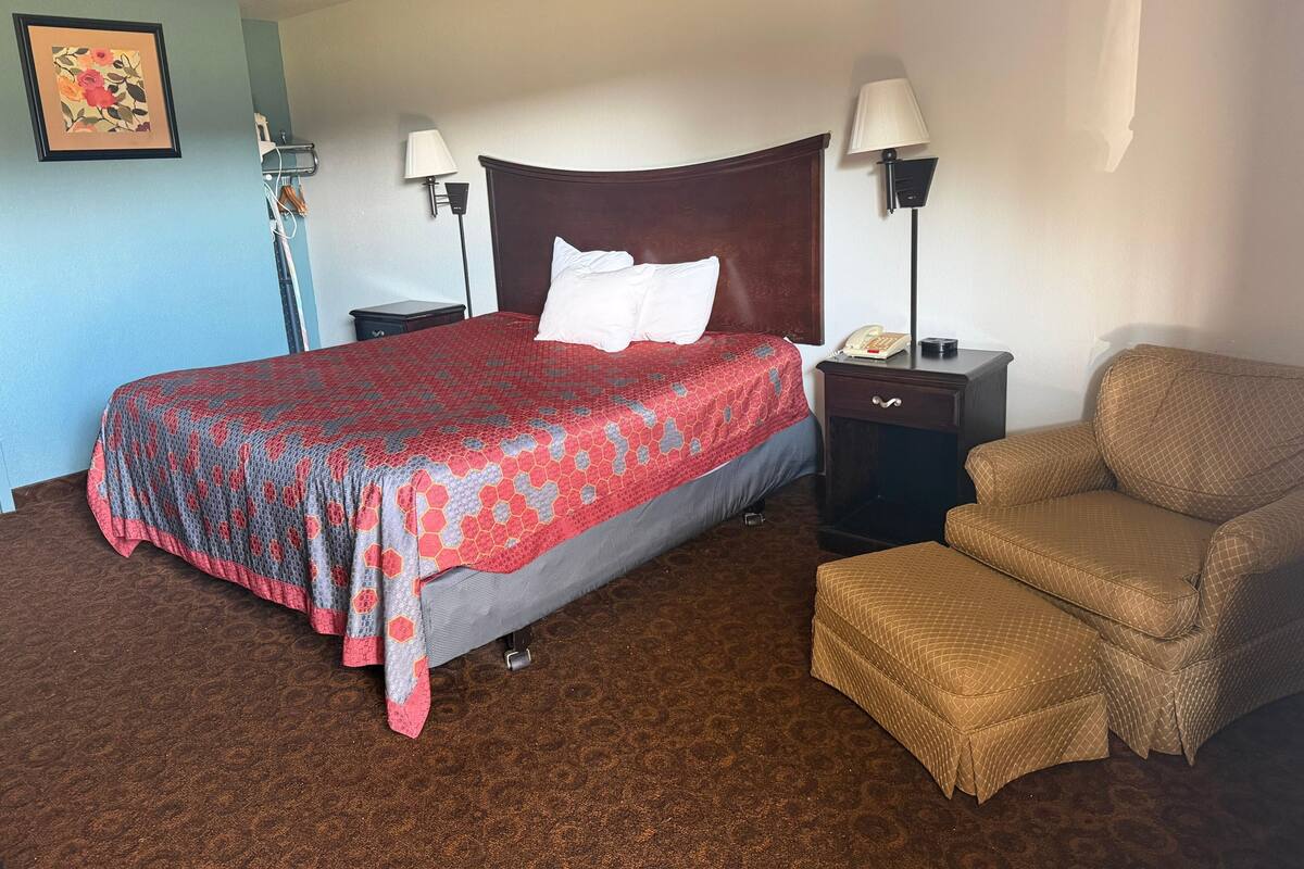 A hotel room with a bed, two bedside tables, a chair, and a lamp.