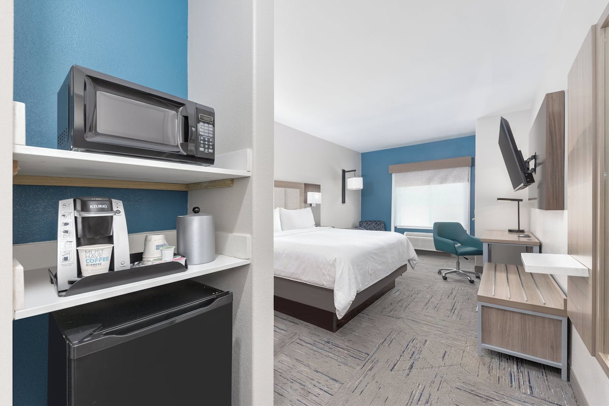 A hotel room with a bed, a desk, a microwave, a coffee maker, and a TV.