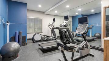 Un gimnasio con equipo de ejercicio, un muro espejado y una pared azul de acento.