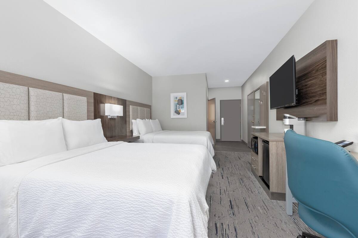 A hotel room with two beds, a desk with a chair, a television, and a bathroom visible through an open door.
