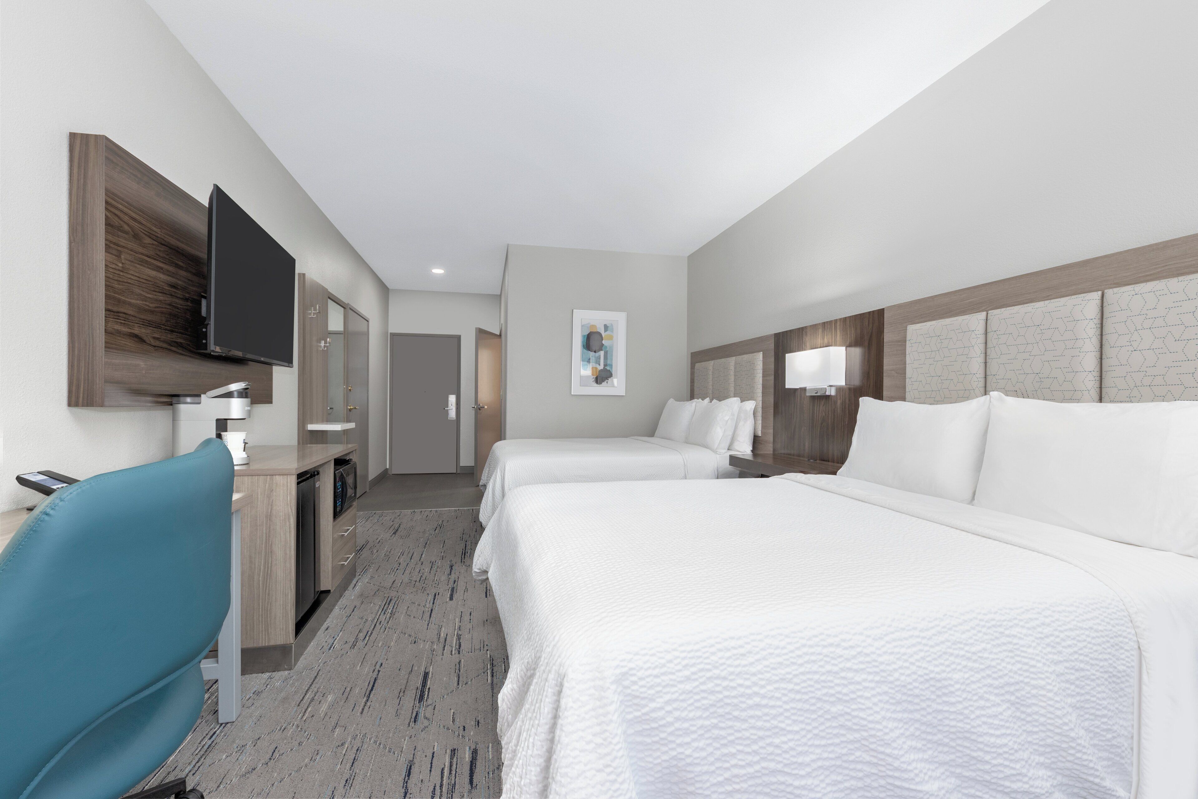 A hotel room with two beds, a desk with a chair, a flat-screen TV mounted on the wall, and a painting on the wall.