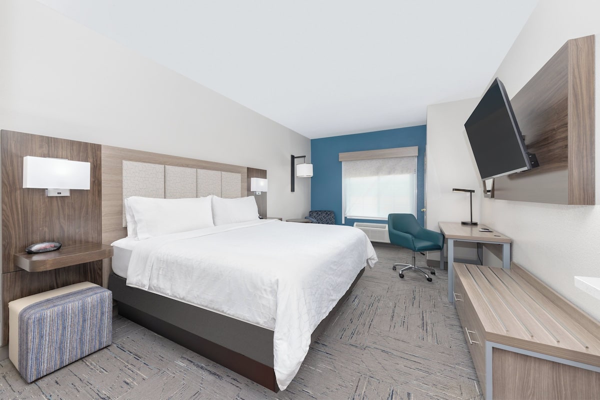 A modern hotel room with a large bed, a desk, a chair, and a TV.