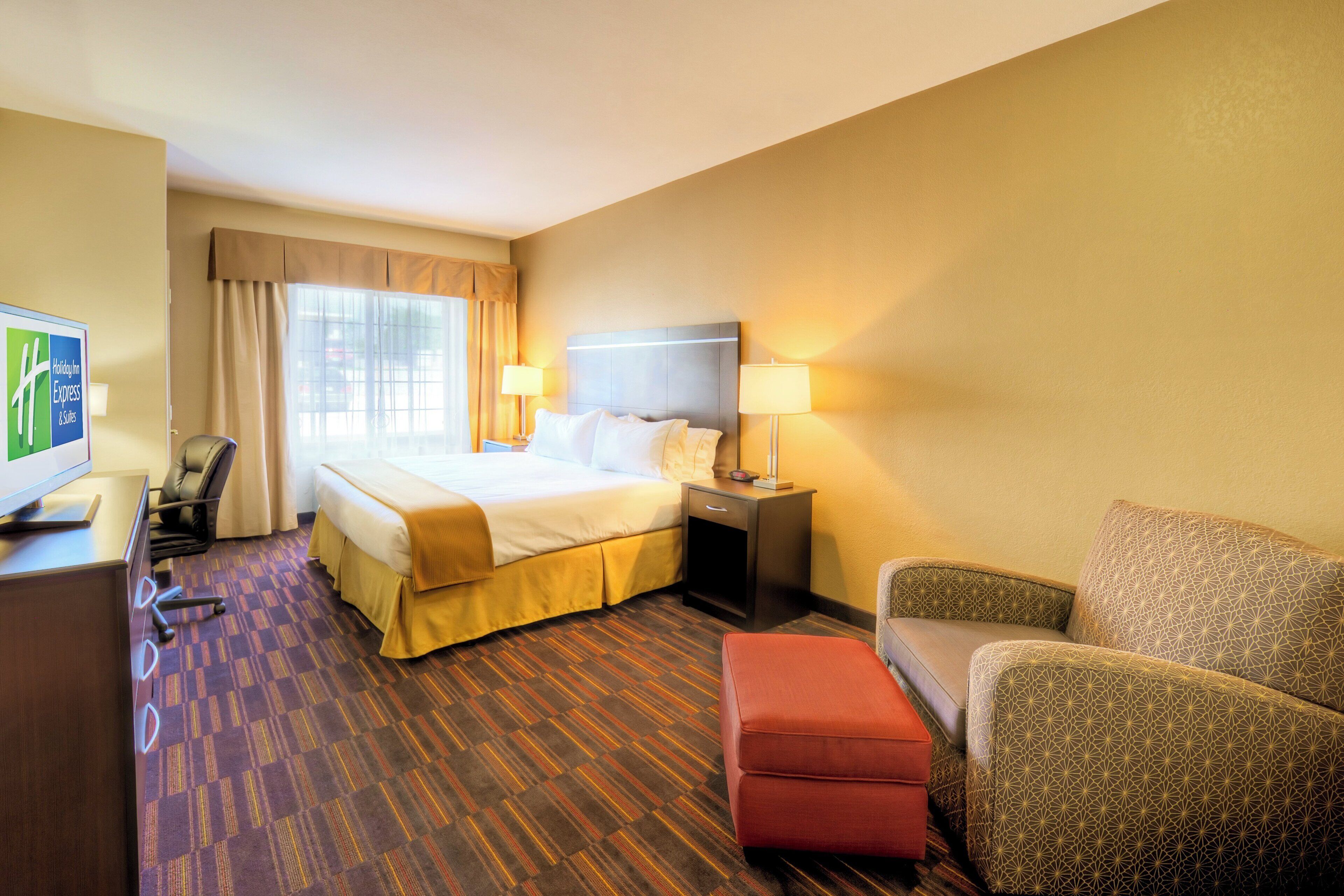 A hotel room with a bed, a desk, a chair, a sofa, and a television.