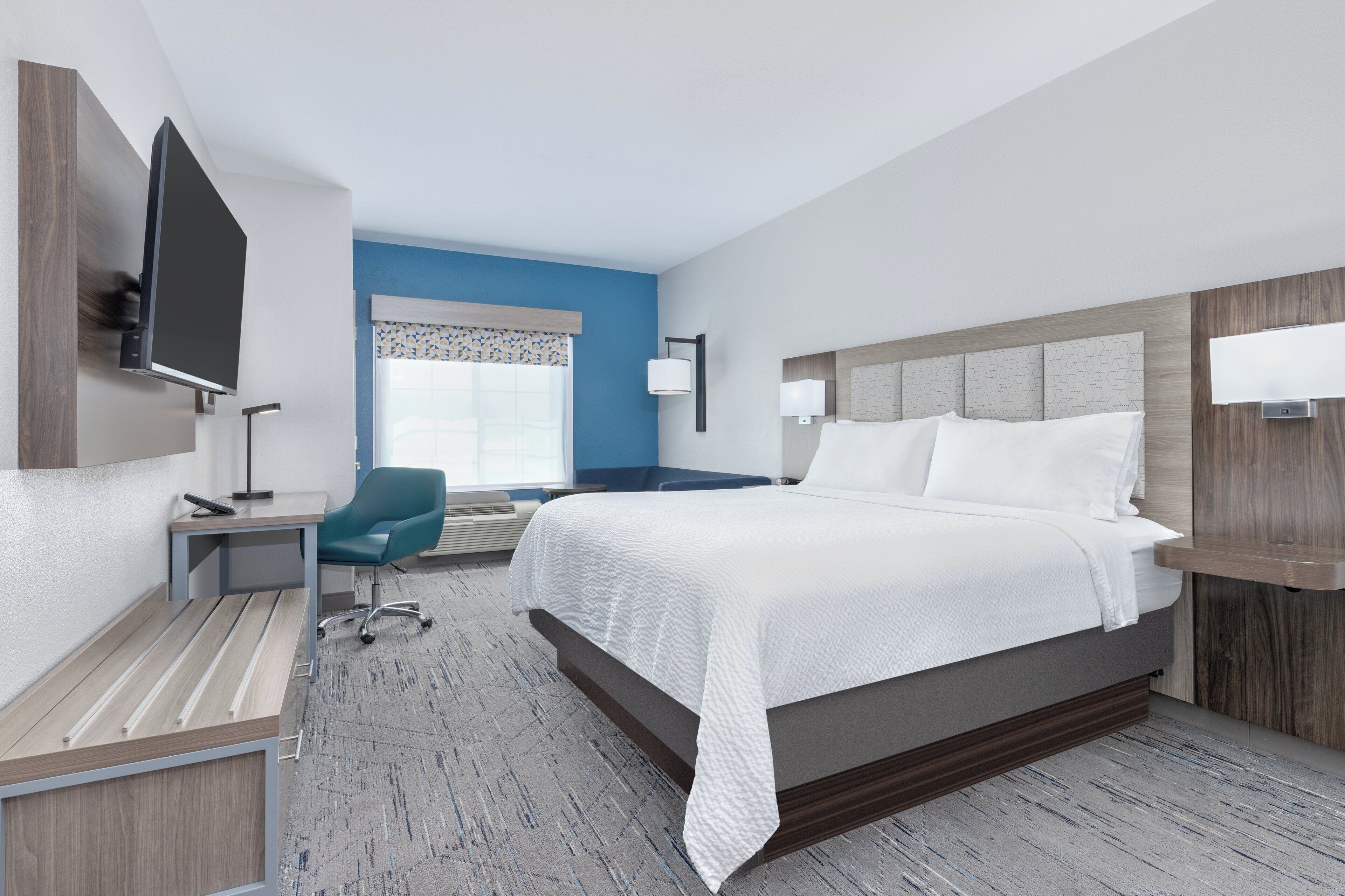 Une chambre d’hôtel moderne dotée d’un grand lit, d’un bureau, d’une chaise, d’un téléviseur à écran plat et d’une fenêtre offrant une vue agréable.