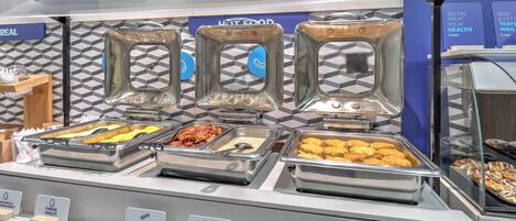Un bufé con diversas opciones de comida, incluyendo huevos, tocino, queso, salchicha y productos de pastelería.