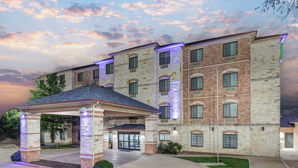 A multi-story hotel with a brick facade, a covered entrance, and a well-maintained lawn.