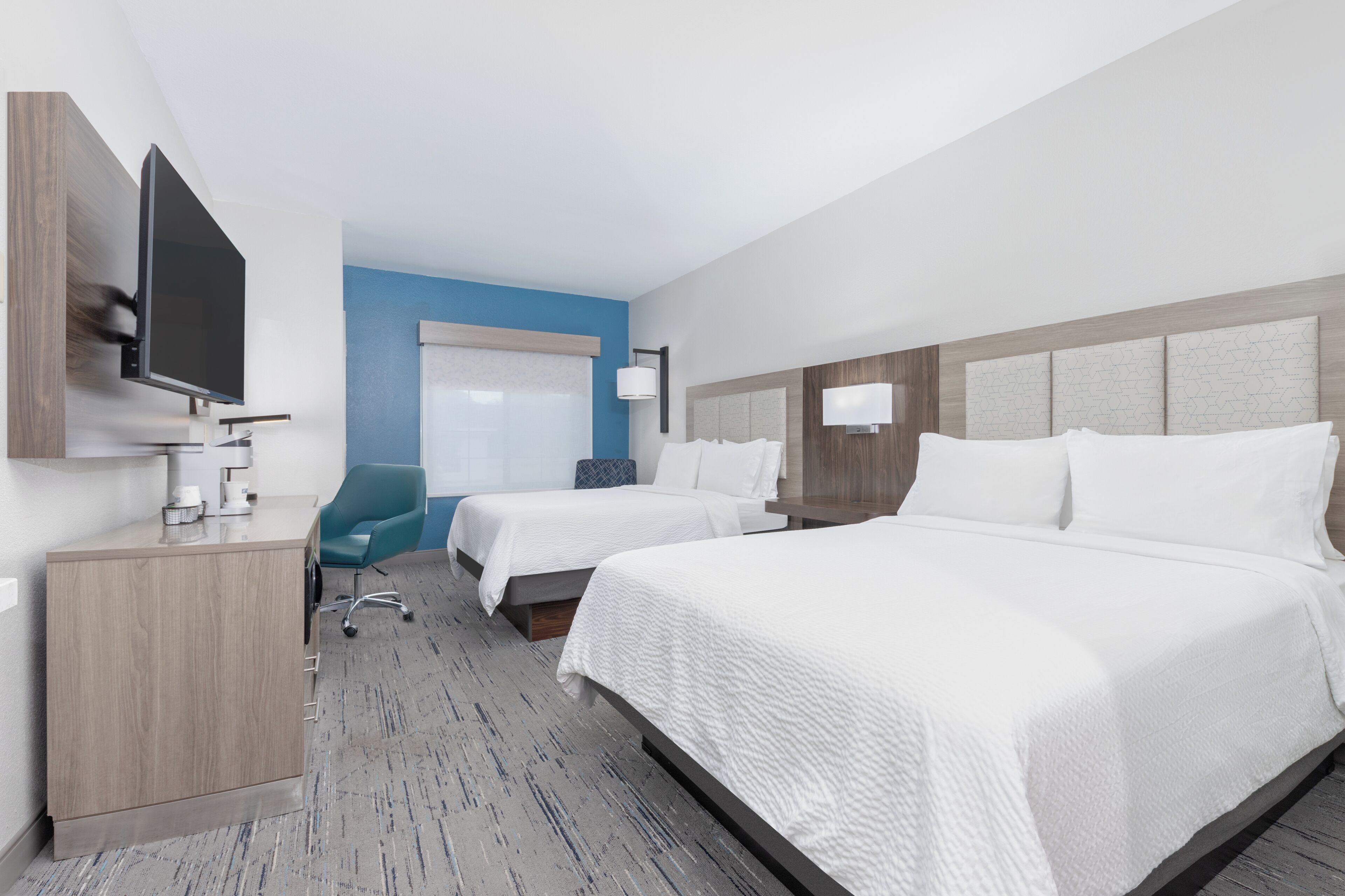 A hotel room with two beds, a desk, a TV, and a chair.