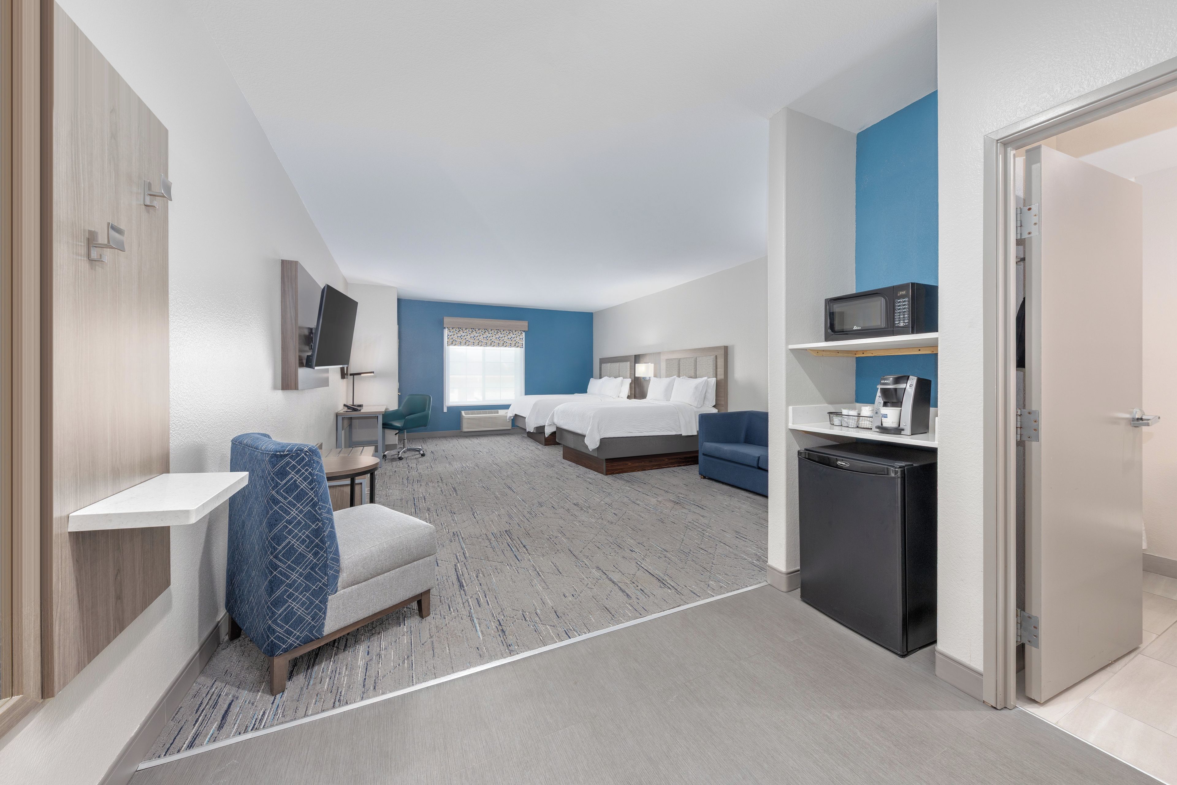 A hotel room with two beds, a desk, a microwave, and a refrigerator.