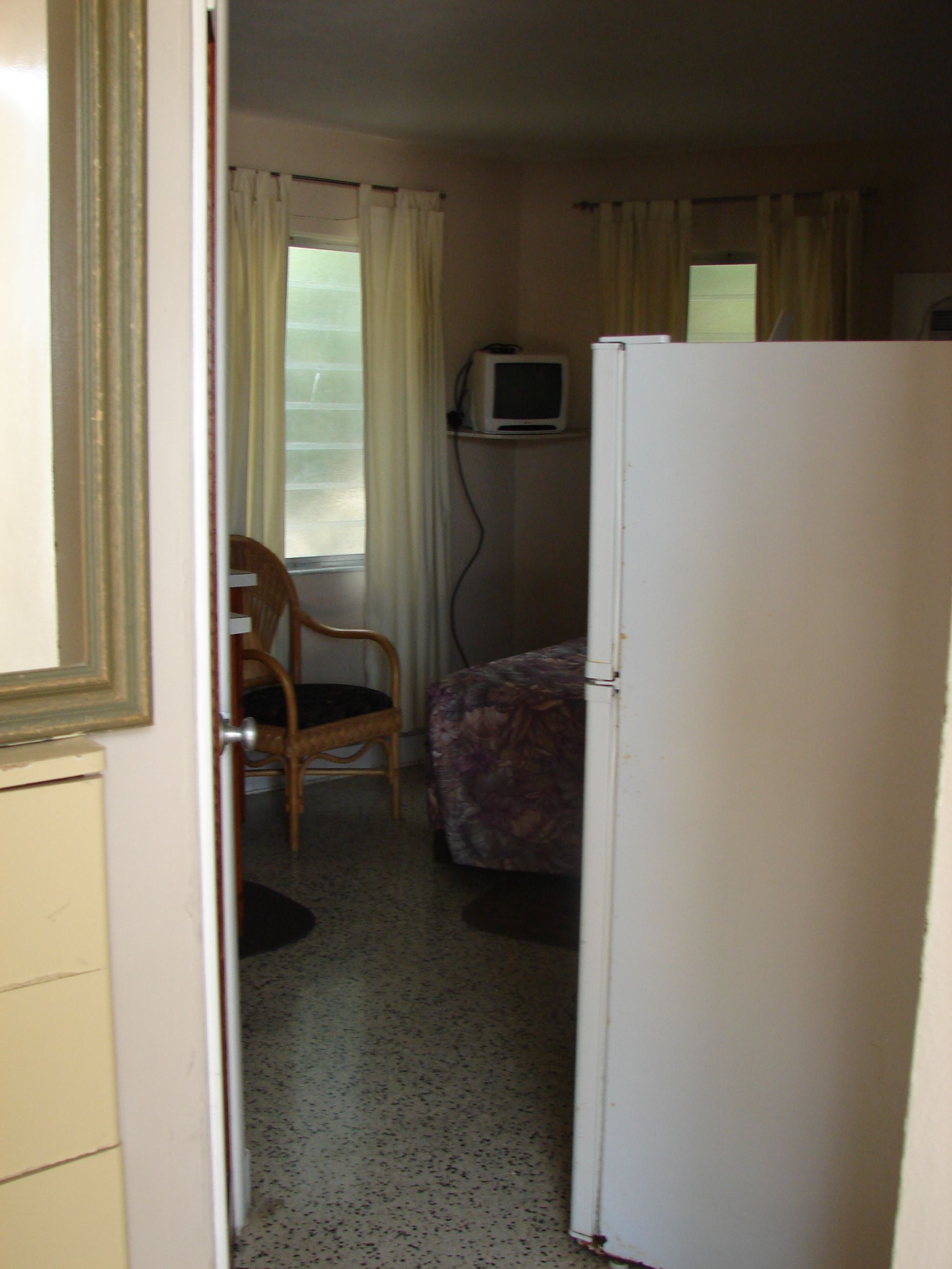 A compact hotel room with a bed, a chair, a small television, and a refrigerator.