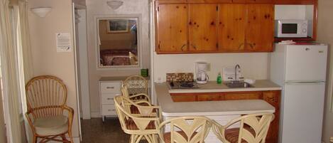 Una cocina compacta con armarios de madera, un microondas, un refrigerador y un pequeño comedor con sillas de mimbre.