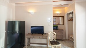 Habitación pequeña con kitchenette, televisión de pantalla plana, escritorio de madera, una silla y armario.