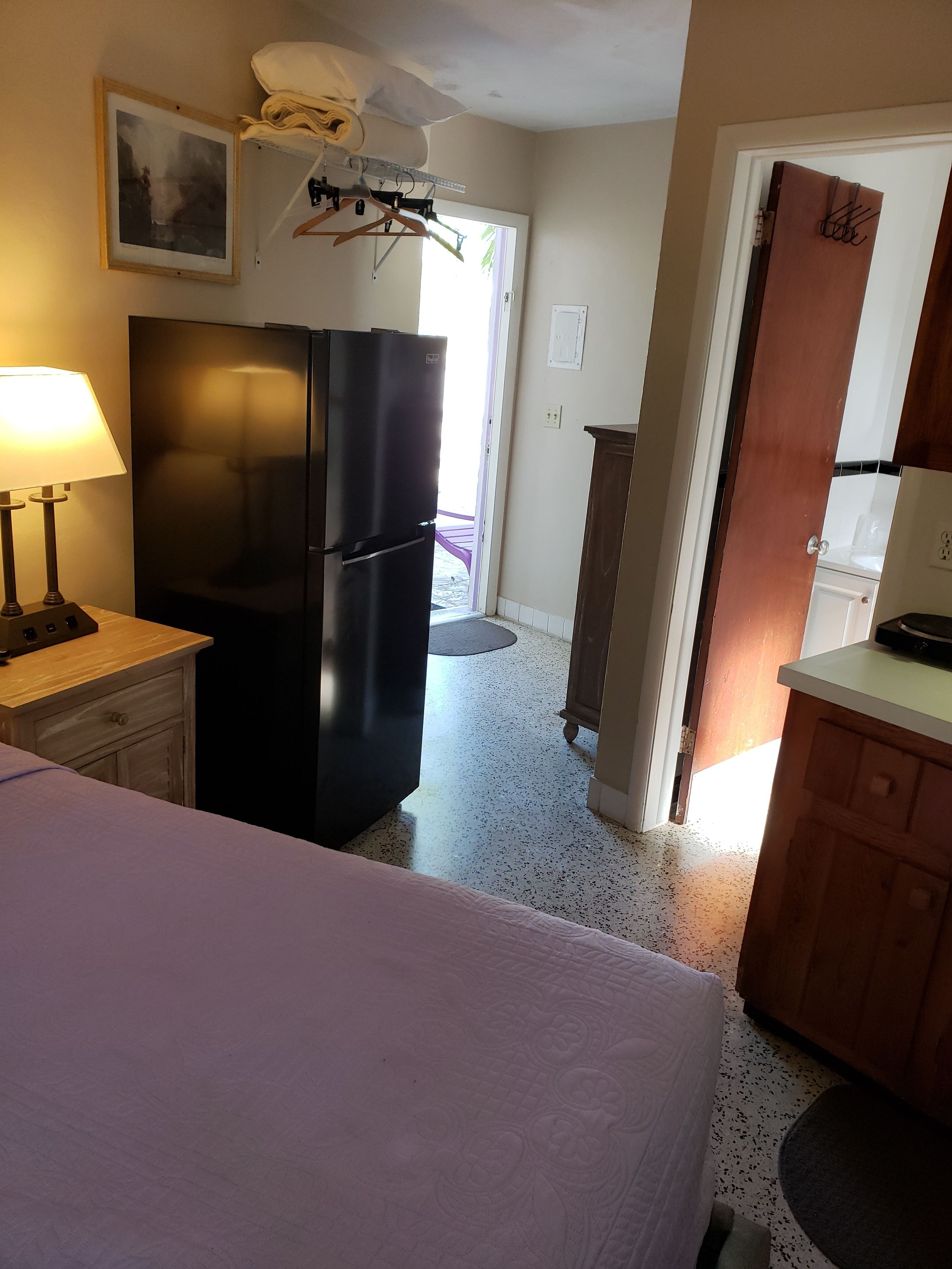 Una cocina compacta con refrigerador, una mesa de comedor y una cama al frente.