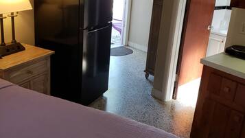 Una cocina compacta con refrigerador, una mesa de comedor y una cama al frente.