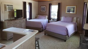 Habitación de hotel con dos camas, un escritorio, una silla, un televisor y un ventanal con cortinas.