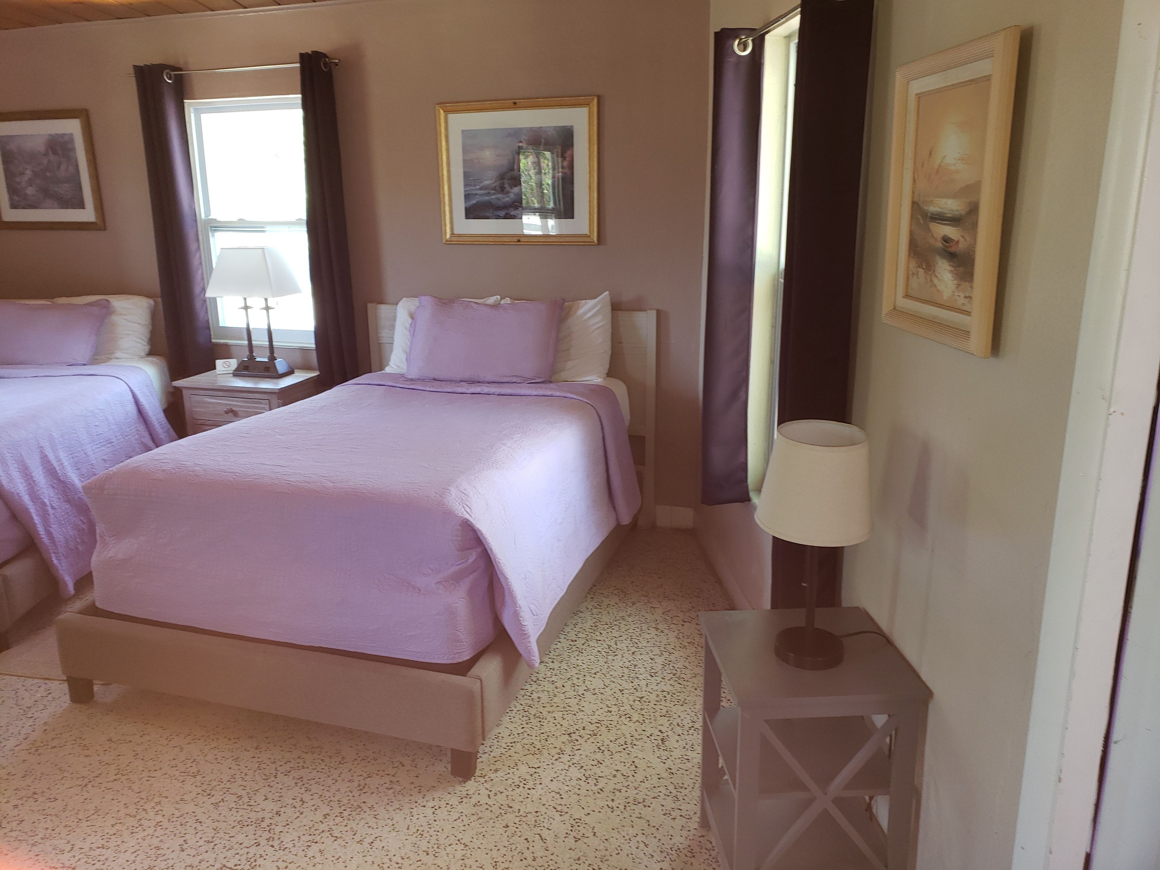 A bedroom with two beds, a nightstand with a lamp, and a framed picture on the wall.