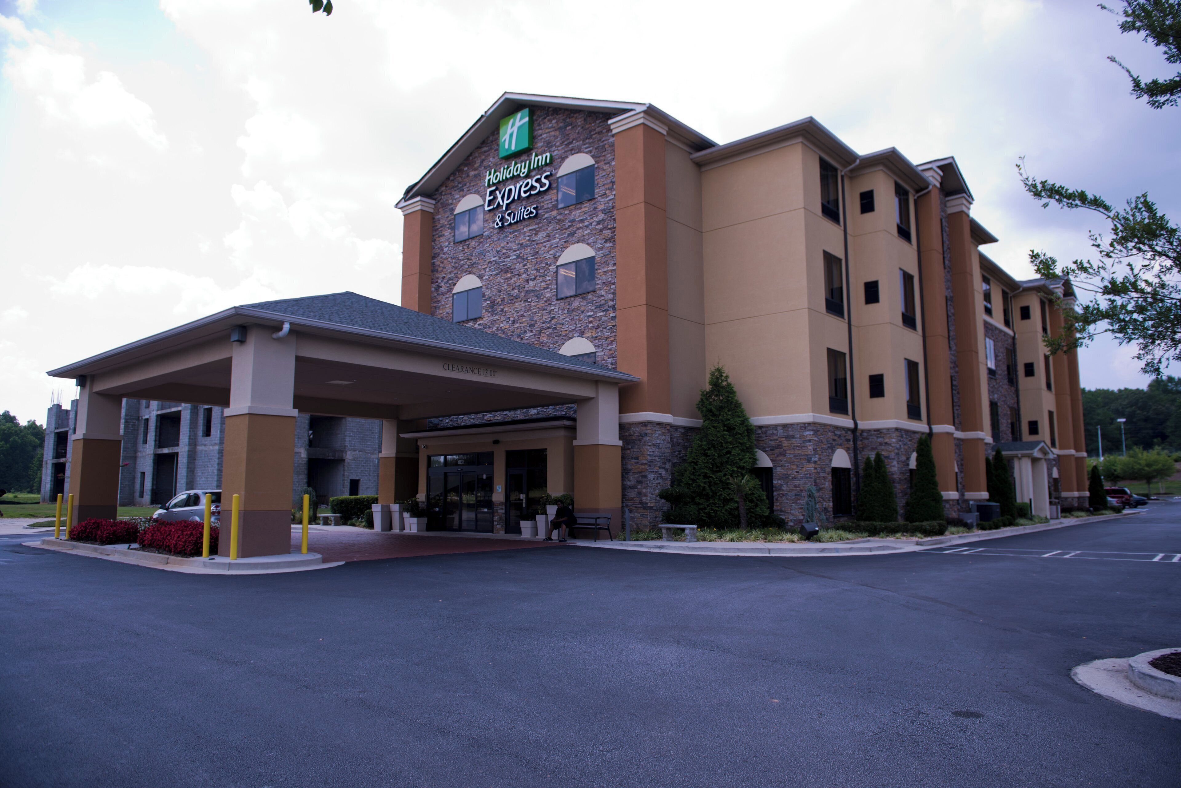 Un hotel Holiday Inn Express & Suites amb entrada coberta, un aparcament i un cel serè.