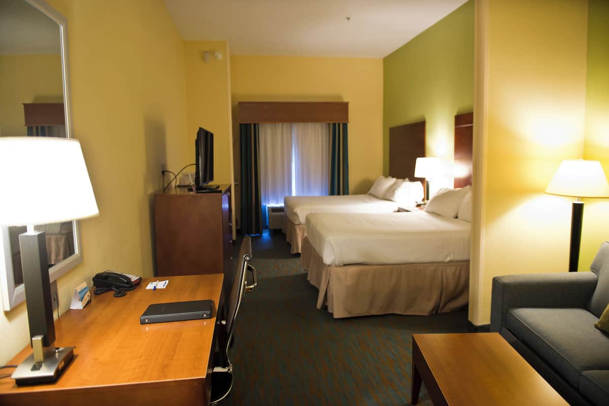 A hotel room with two beds, a desk with a telephone, a television, and a sofa.