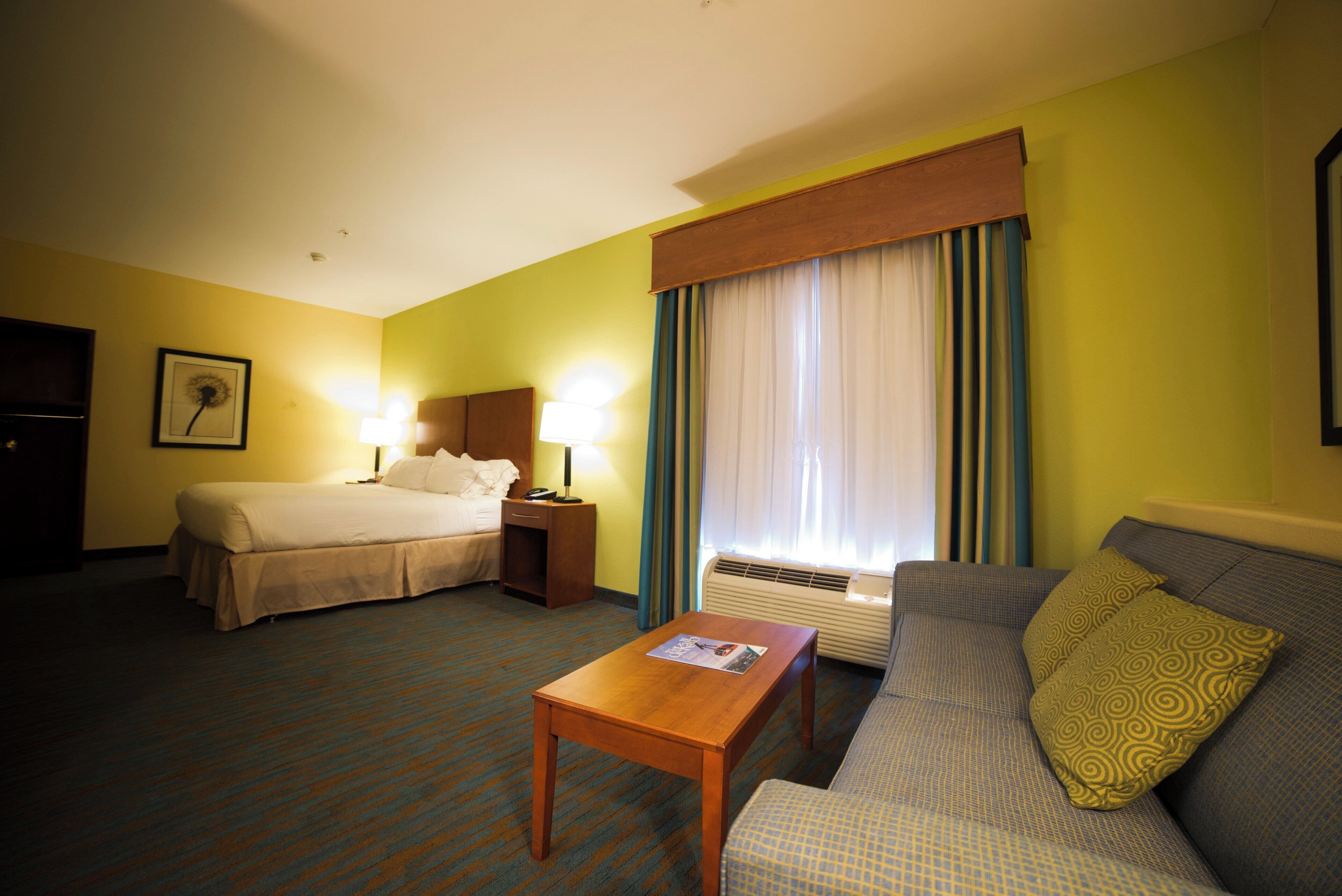A hotel room with a bed, a sofa, a table, and a window with curtains.