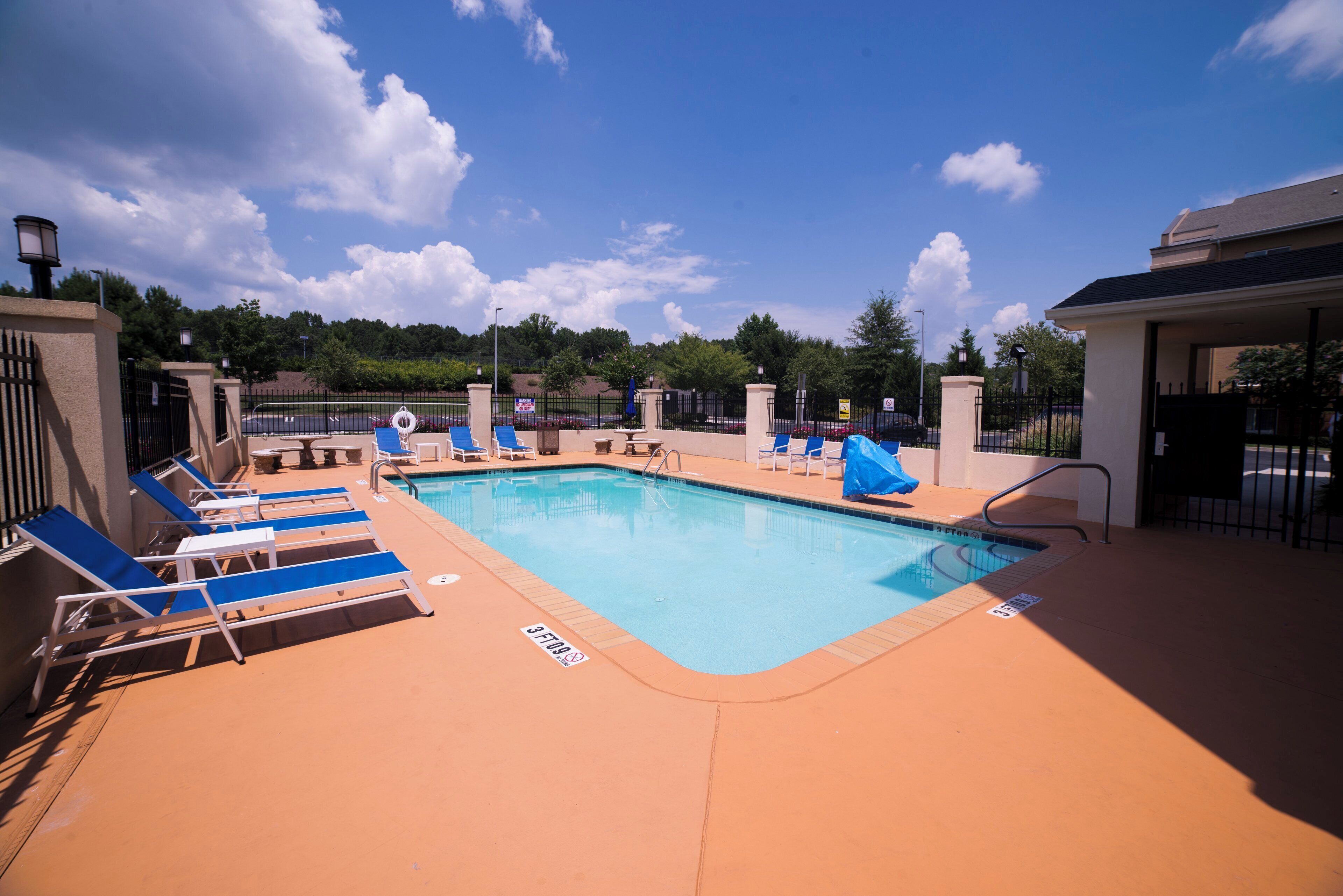 A swimming pool with lounge chairs and a lifeguard chair, surrounded by a fence and trees.