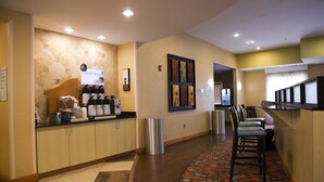 A hotel reception area with a coffee station, seating area, and a trash bin.