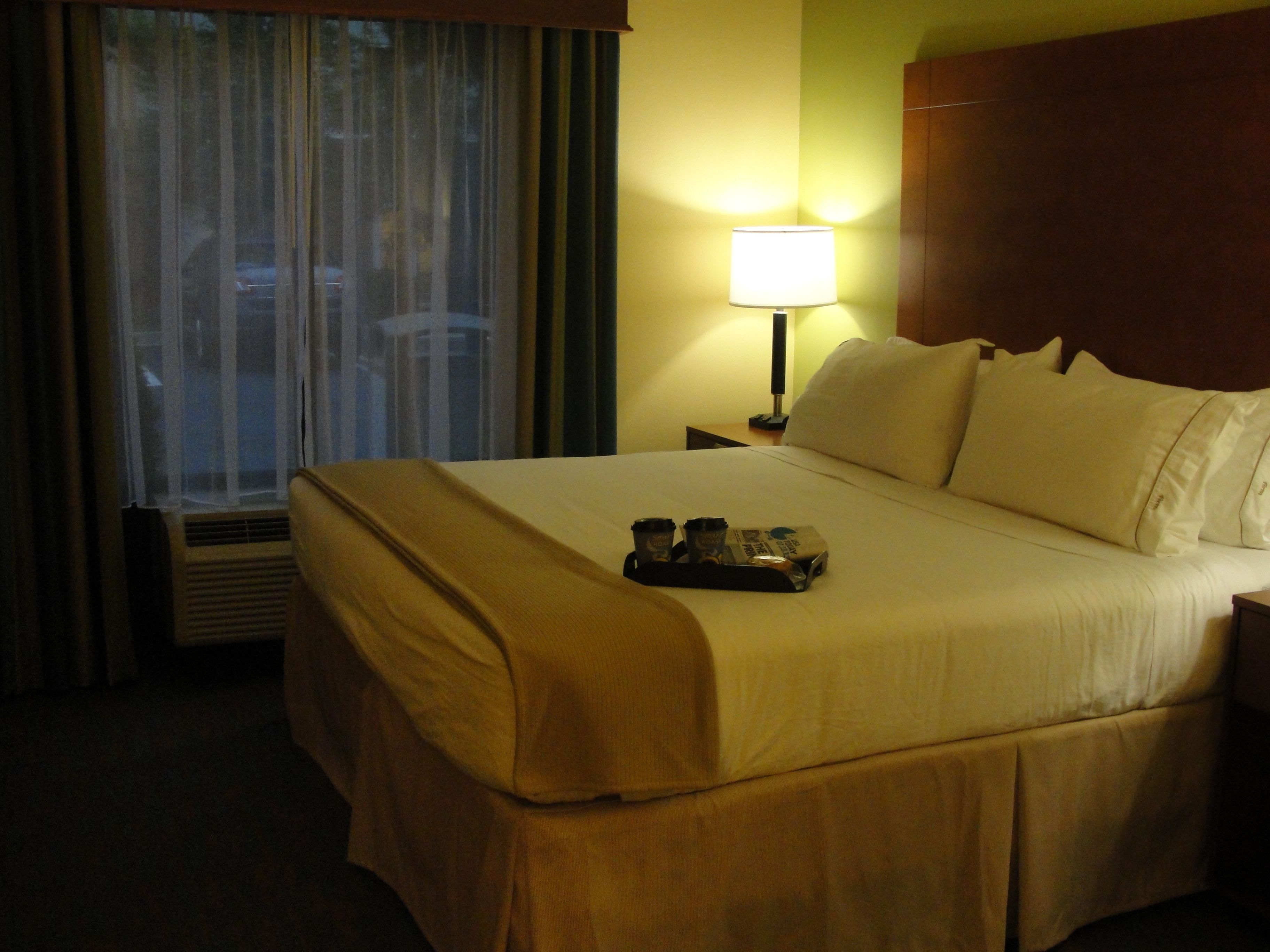 A hotel room with a bed, a nightstand, a lamp, and a window with curtains.